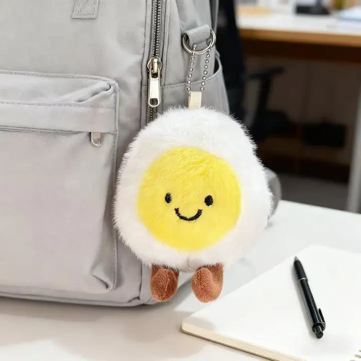 Fluffy boiled egg plush charm clipped to a gray backpack zipper