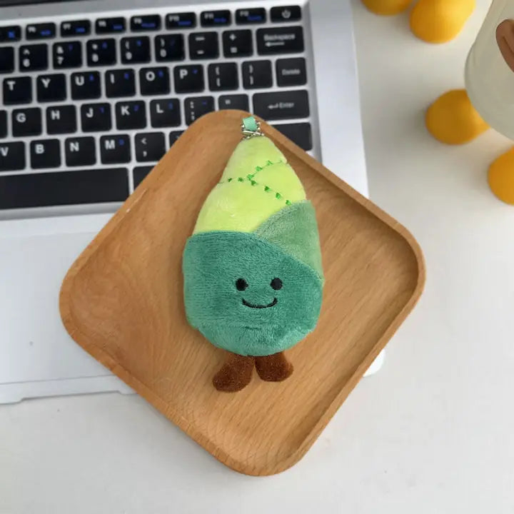 Bamboo shoot plush keychain charm with smiling face on a wooden tray