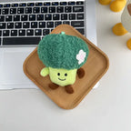 Broccoli plush keychain charm with flower detail and smiling face on a wooden tray