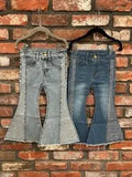 Two pairs of girls bell-bottom jeans in light and dark wash hanging on a brick wall