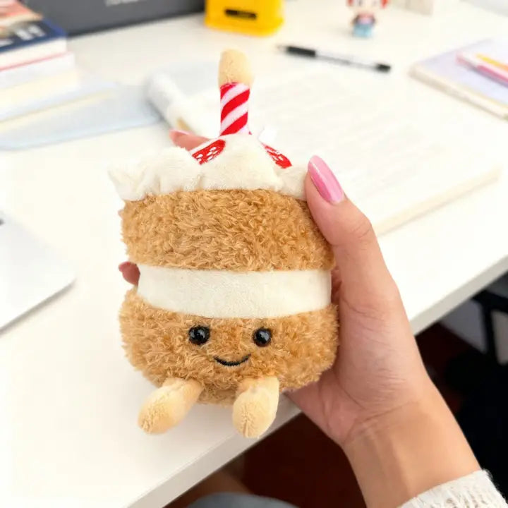 Birthday cake plush charm with candle and frosting layers held in a hand