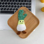 Green onion plush keychain charm with smiling face on a wooden tray