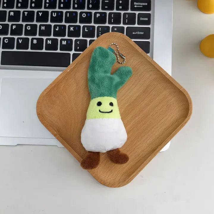 Green onion plush keychain charm with smiling face on a wooden tray