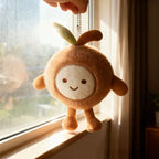 Brown coconut plush keychain charm with smiling face hanging from a ball chain