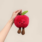 Red apple plush keychain charm with leaf and corduroy legs held up by hand