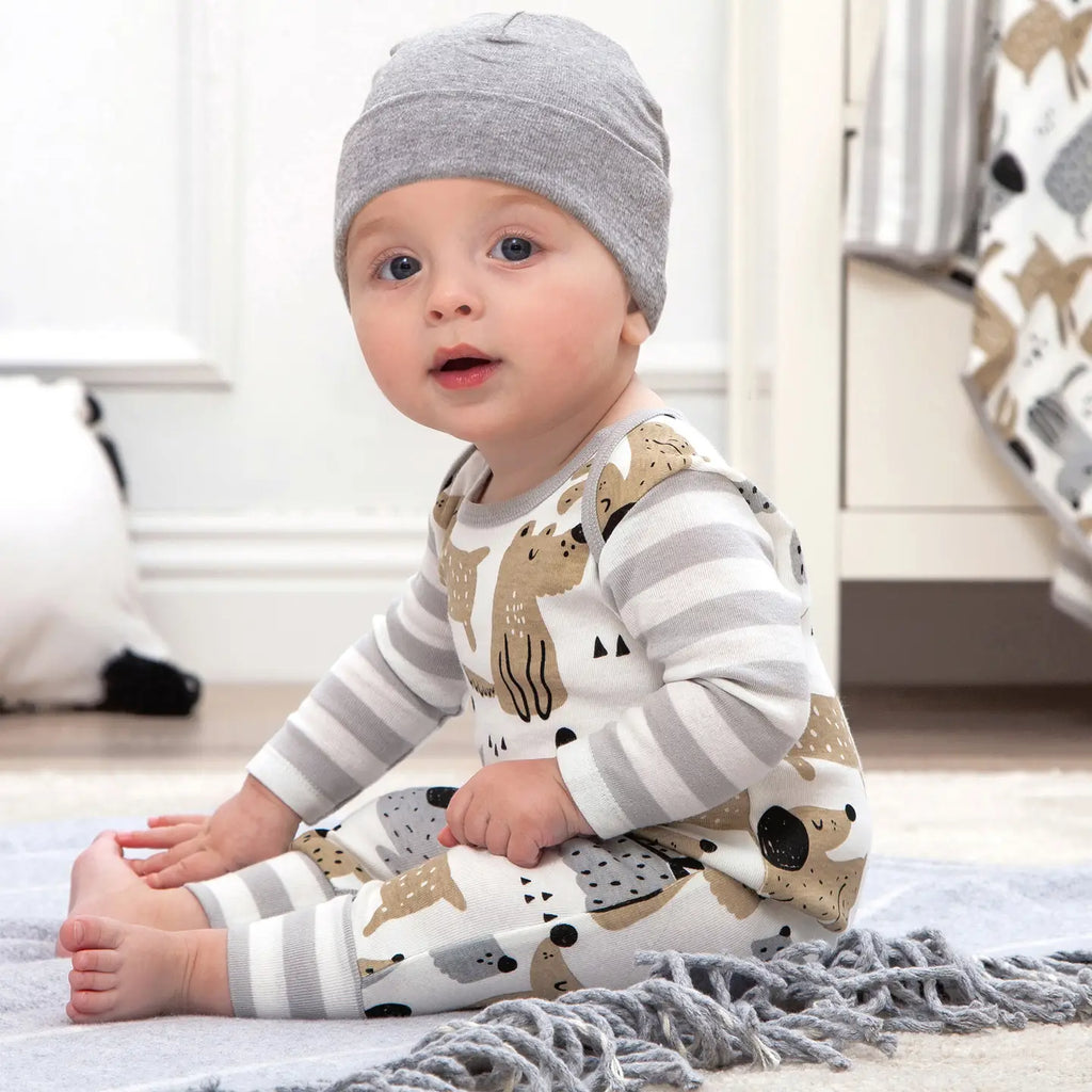 Baby sitting in a puppy dog print romper with gray striped sleeves and a gray knit hat