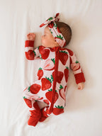 Sleeping newborn in a pink strawberry print zip romper and headband, full length