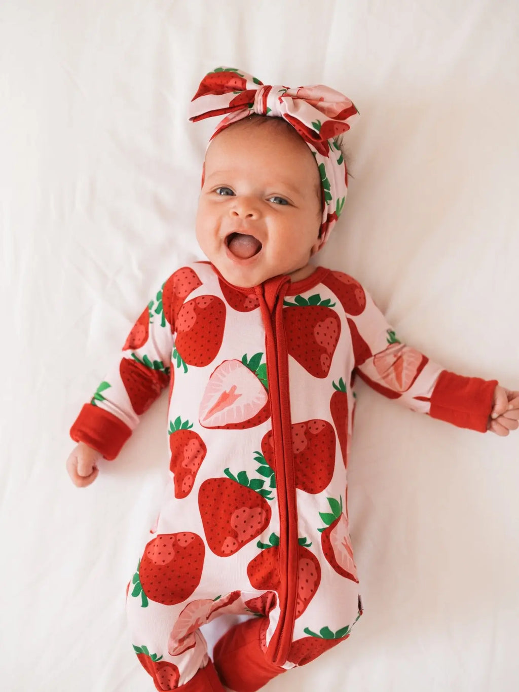 Smiling baby in a strawberry print long-sleeve zip romper with matching bow headband