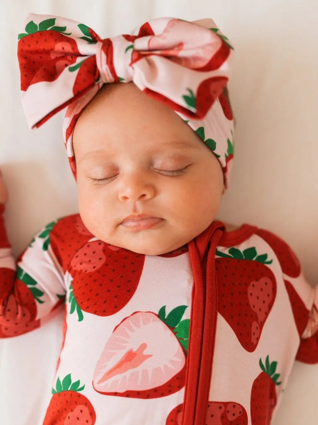 Close-up of sleeping baby in strawberry print bamboo romper with large bow headband
