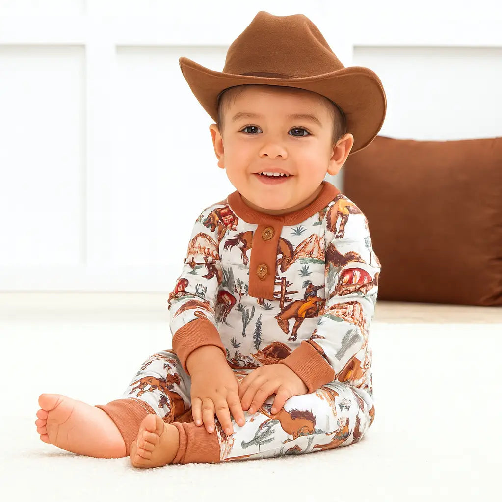 Baby in a cowboy hat wearing the Western print henley romper with brown trim