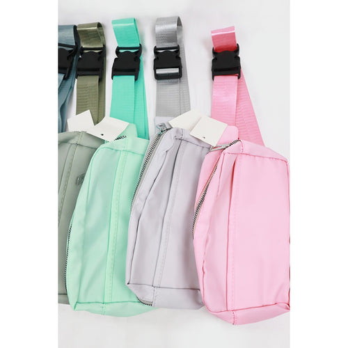 Four crossbody belt bags in sage, mint, light gray, and pink with black clip buckles