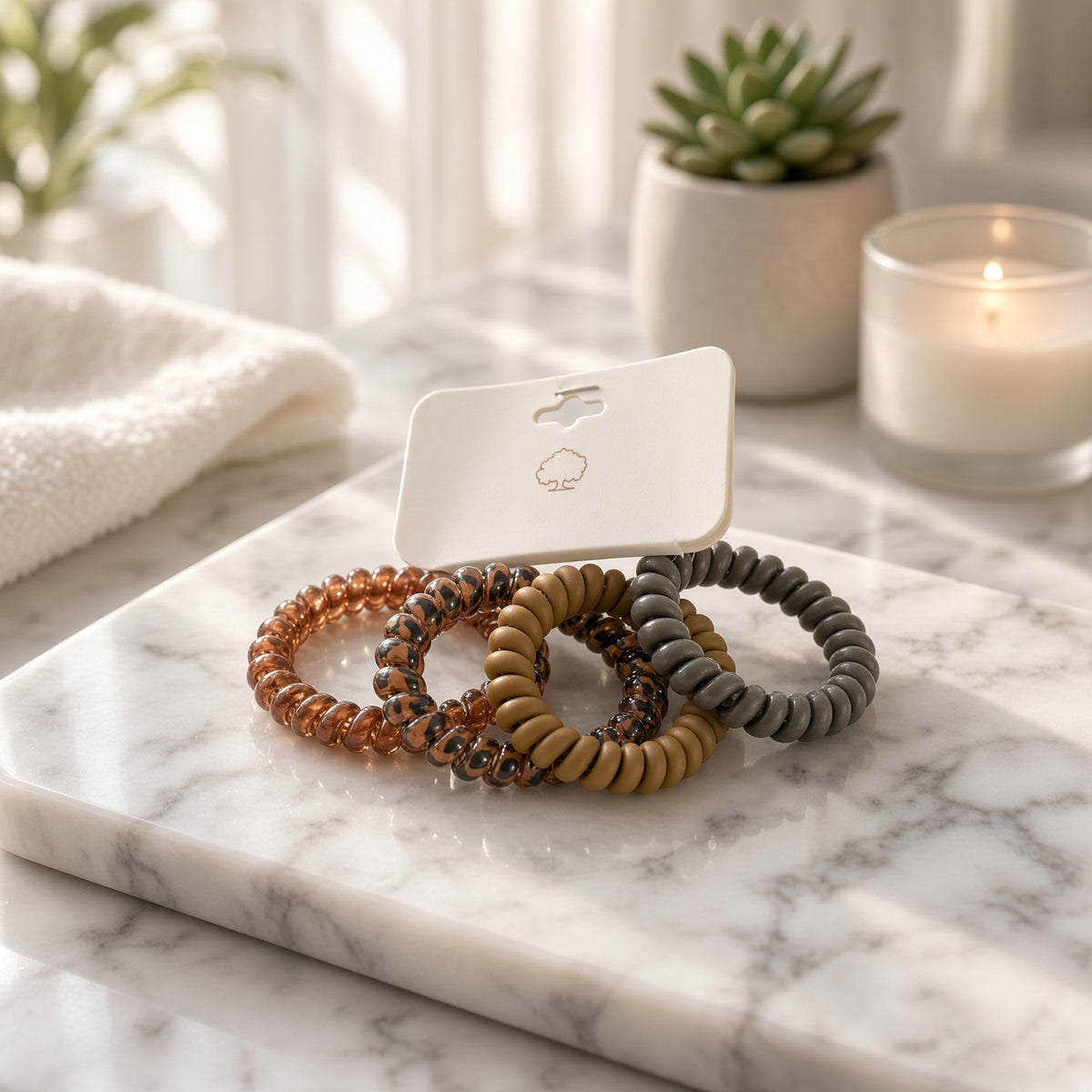 Four spiral coil hair ties in brown and gray tones on a marble tray