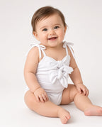 Baby wearing a white one-piece swimsuit with tie straps and front bow