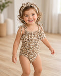 Toddler wearing a tan floral ruffle tie-shoulder onesie with matching knotted headband