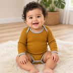 Smiling baby sitting in a mustard long-sleeve ribbed onesie