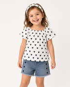 Girl wearing a white heart print flutter-sleeve top, denim shorts, and heart headband