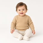 Smiling baby sitting in a light caramel chunky knit crewneck sweater