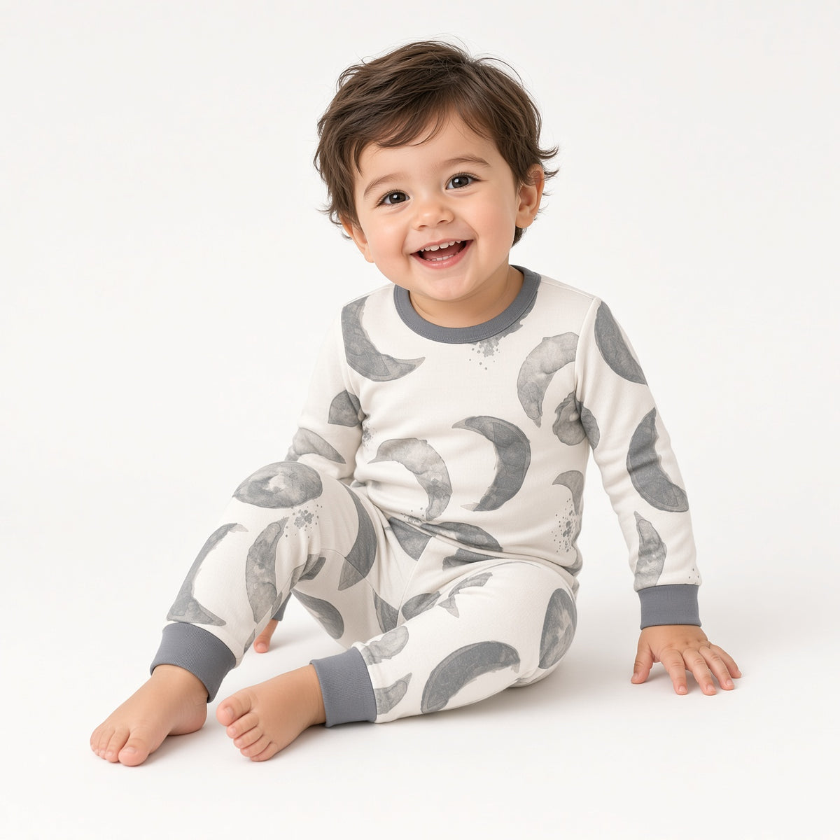 Toddler sitting in gray moon print two-piece pajamas