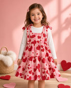 Girl wearing a red heart print tie-shoulder tiered pinafore dress over a white top