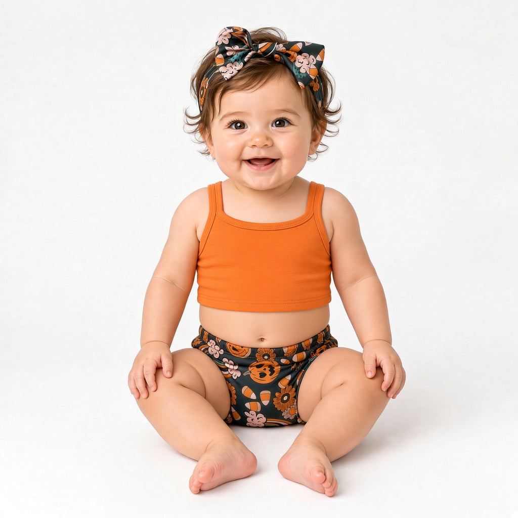 Baby wearing Halloween pumpkin print bummies and bow headband with an orange top
