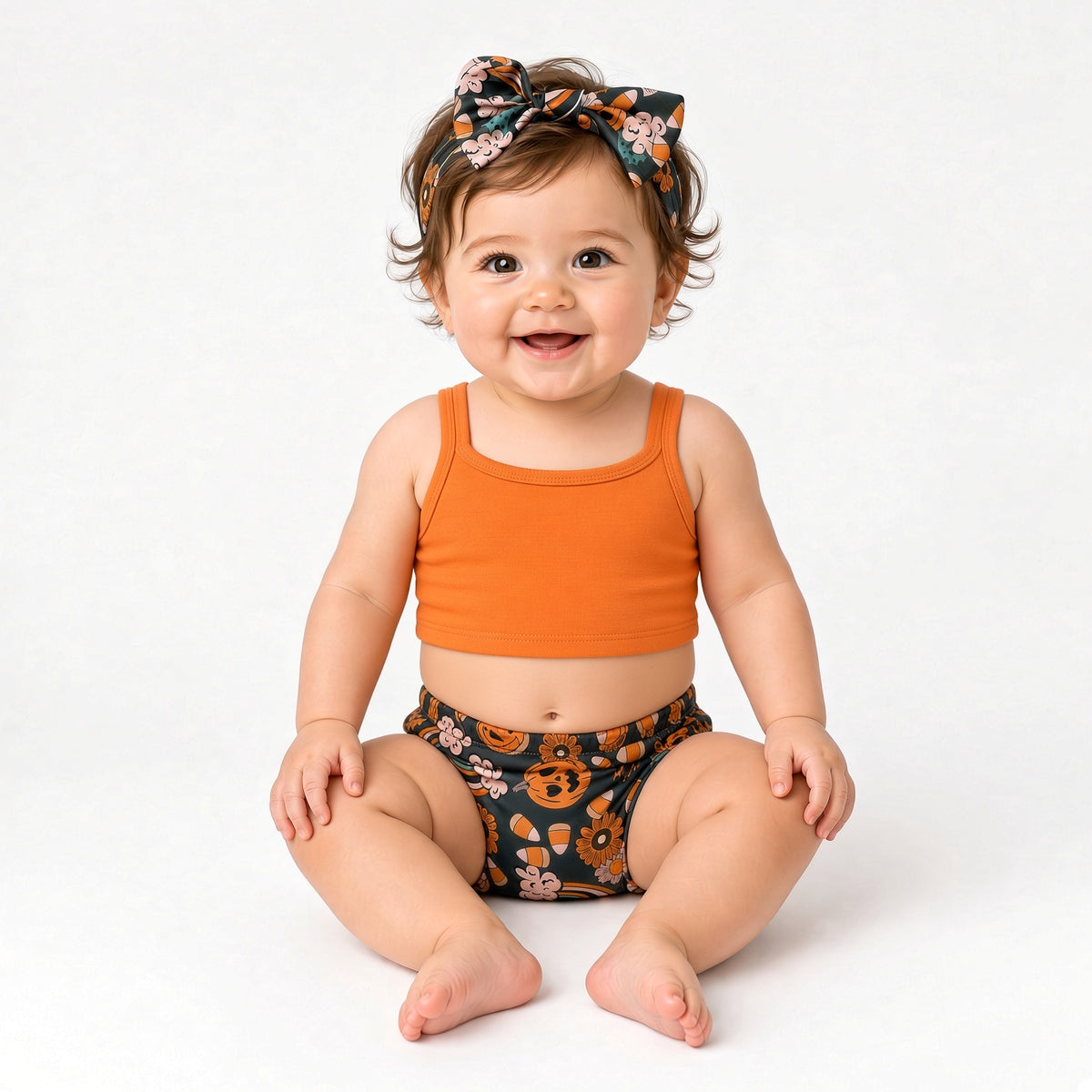 Baby wearing Halloween pumpkin print bummies and bow headband with an orange top