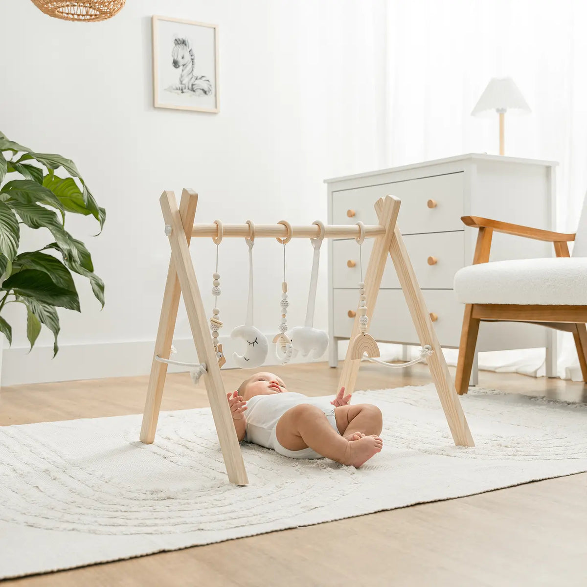 Baby lying on a rug under the Comfy Cubs wooden play gym with hanging sensory toys