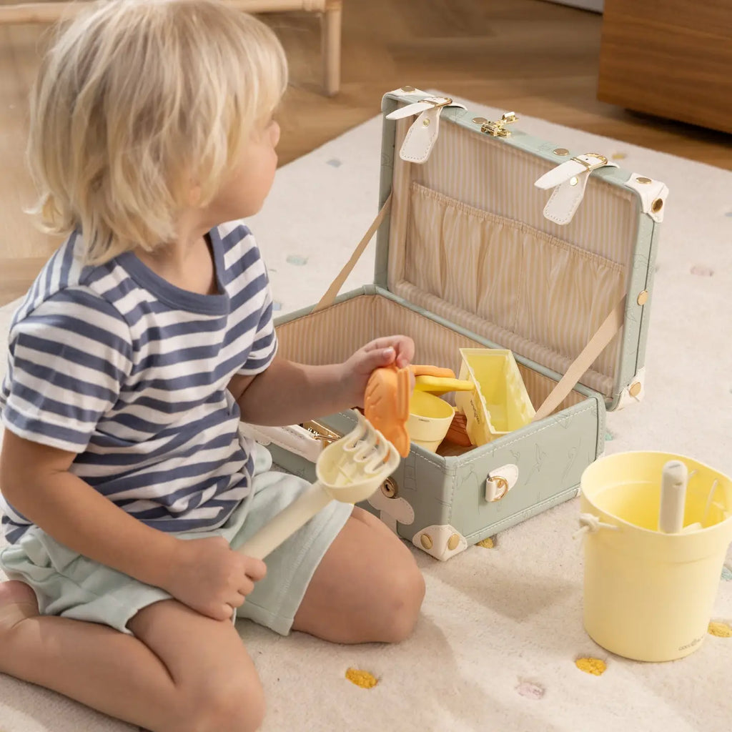 Child packing toys into the open Coco Village ocean play suitcase