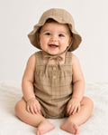 Baby wearing a brown plaid sleeveless romper with matching bonnet-style hat