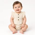Smiling baby sitting in a cream eyelet flutter-sleeve bubble romper with brown buttons