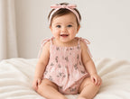 Baby wearing the pink floral Libby romper with tie straps and matching headband