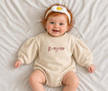 Baby wearing a cream Bonjour embroidered puff-sleeve romper with headband