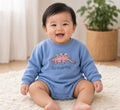 Baby wearing a light blue T-Rex romper with pink stegosaurus graphic