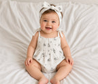 Baby wearing the white floral Libby romper with tie shoulders and bow headband