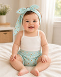 Baby wearing a white tank and teal daisy print bottoms with matching head wrap