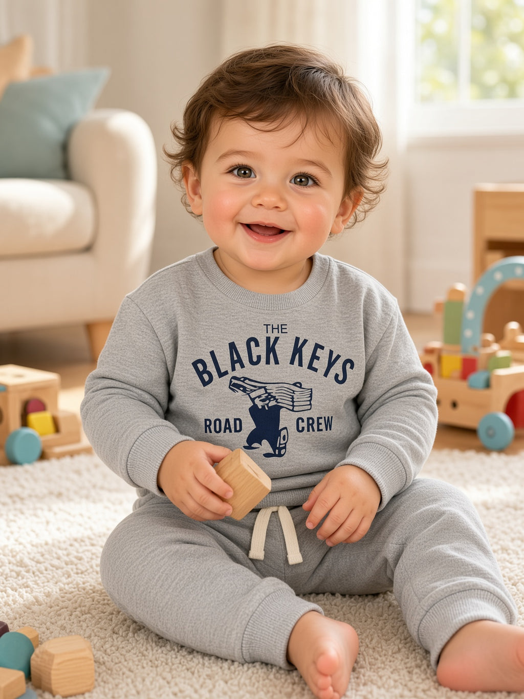 Toddler sitting in a light gray The Black Keys Road Crew sweatshirt and drawstring pants