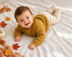 Baby lying on tummy in a mustard yellow chunky knit sweater with fall leaves nearby