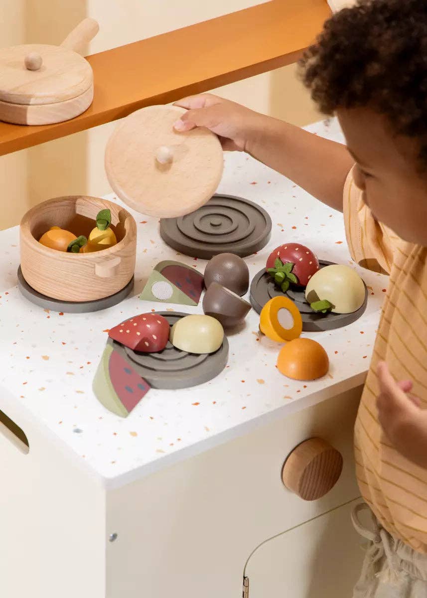 Child playing with wooden play fruits and pots at a toy kitchen